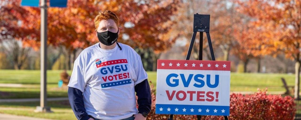 Sam Jacobs standing next to sign that reads "GVSU Votes!"